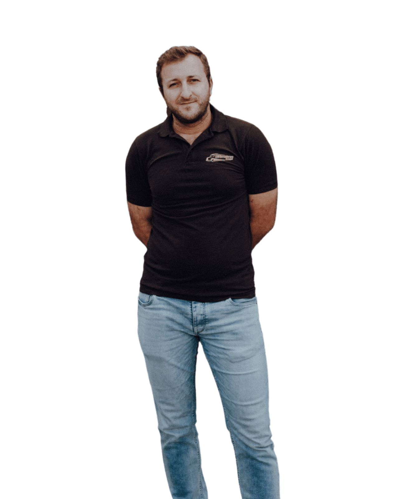 Mann in schwarzem Poloshirt und blauen Jeans, Hände hinter dem Rücken verschränkt, leicht zur Seite gedreht.
