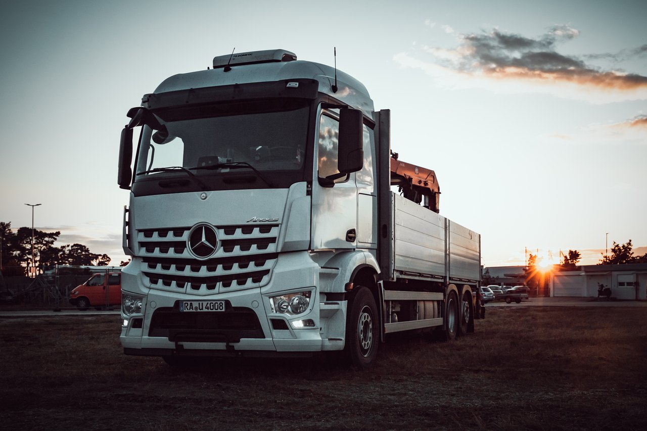 Weißer Mercedes-Benz LKW mit Pritsche und Ladekran bei Sonnenuntergang.